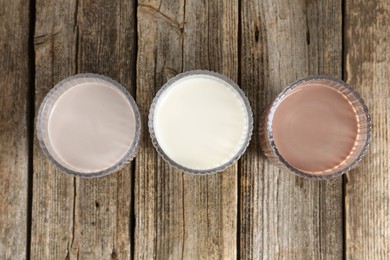 Photo of Different tasty protein cocktails in glasses on wooden table, flat lay