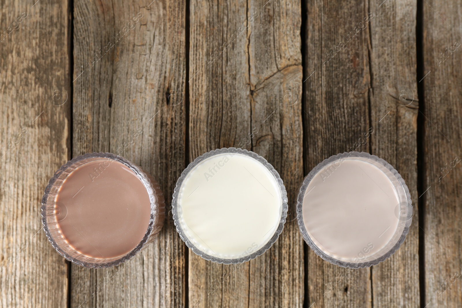 Photo of Different tasty protein cocktails in glasses on wooden table, flat lay. Space for text