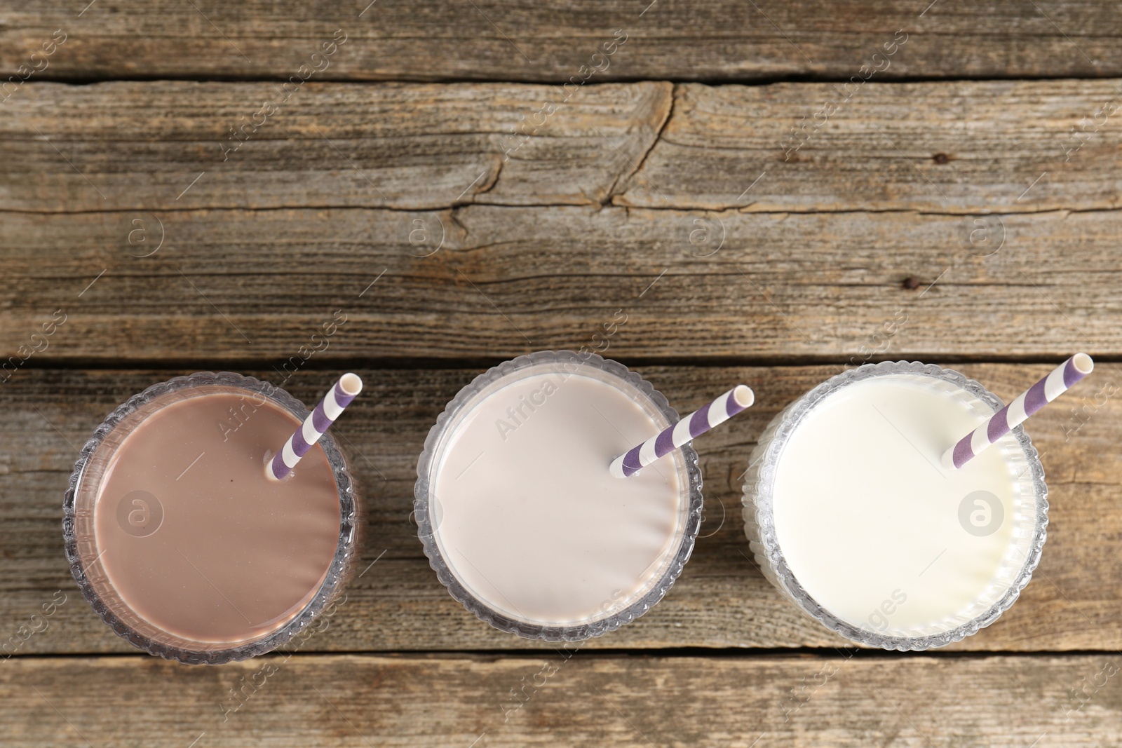 Photo of Different tasty protein cocktails in glasses on wooden table, flat lay. Space for text