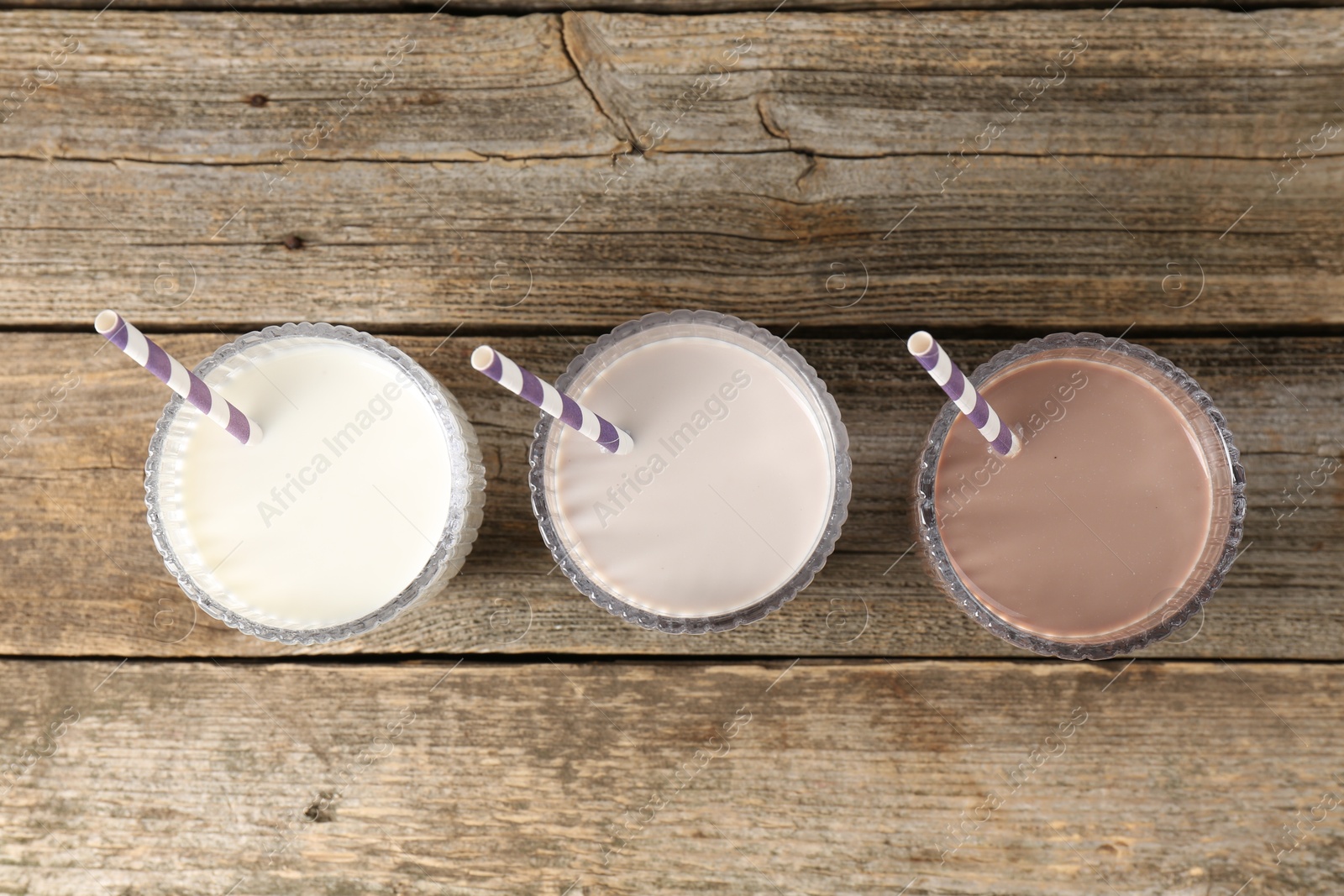 Photo of Different tasty protein cocktails in glasses on wooden table, flat lay