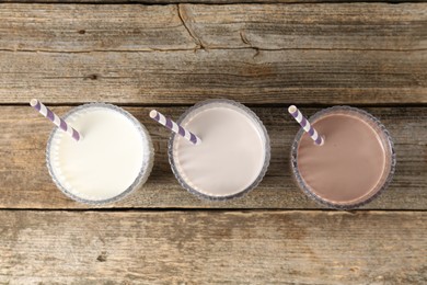 Photo of Different tasty protein cocktails in glasses on wooden table, flat lay