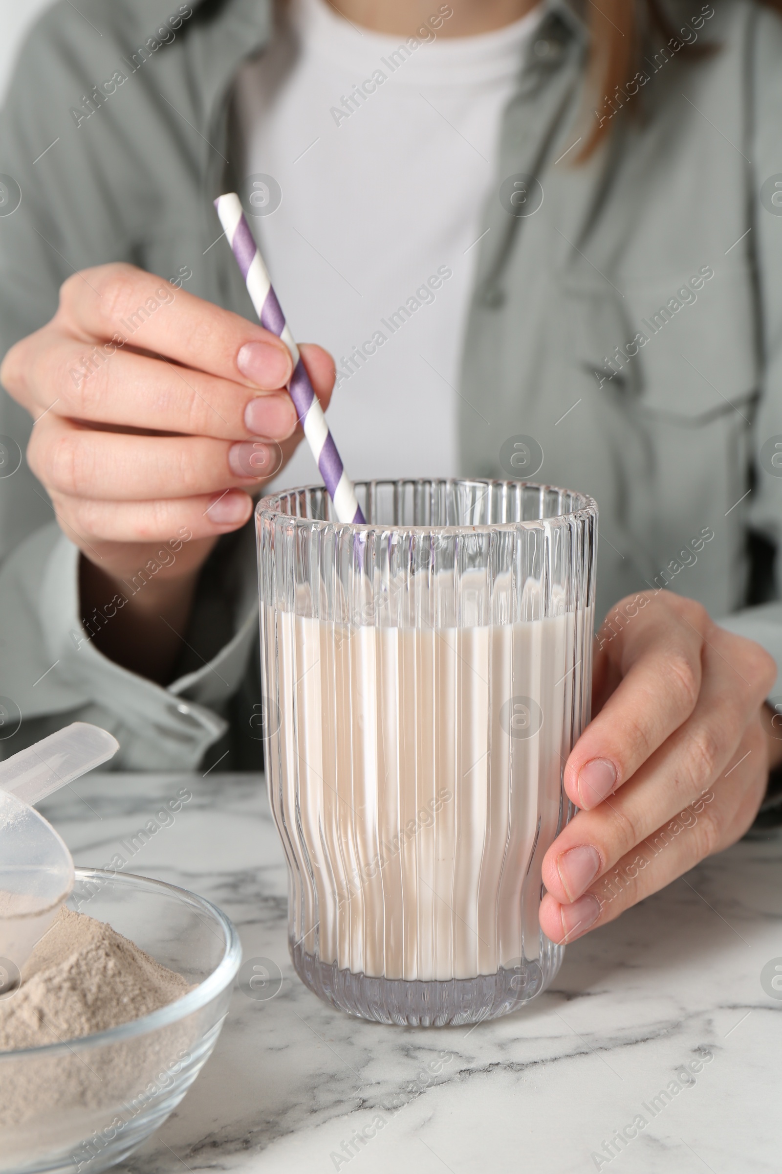 Photo of Woman with glass of protein cocktail at white marble table, closeup