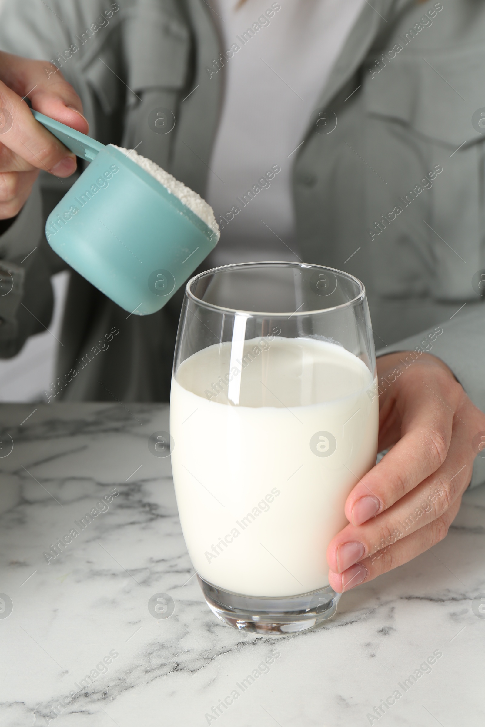 Photo of Making protein cocktail. Woman adding powder into glass with milk at white marble table, closeup