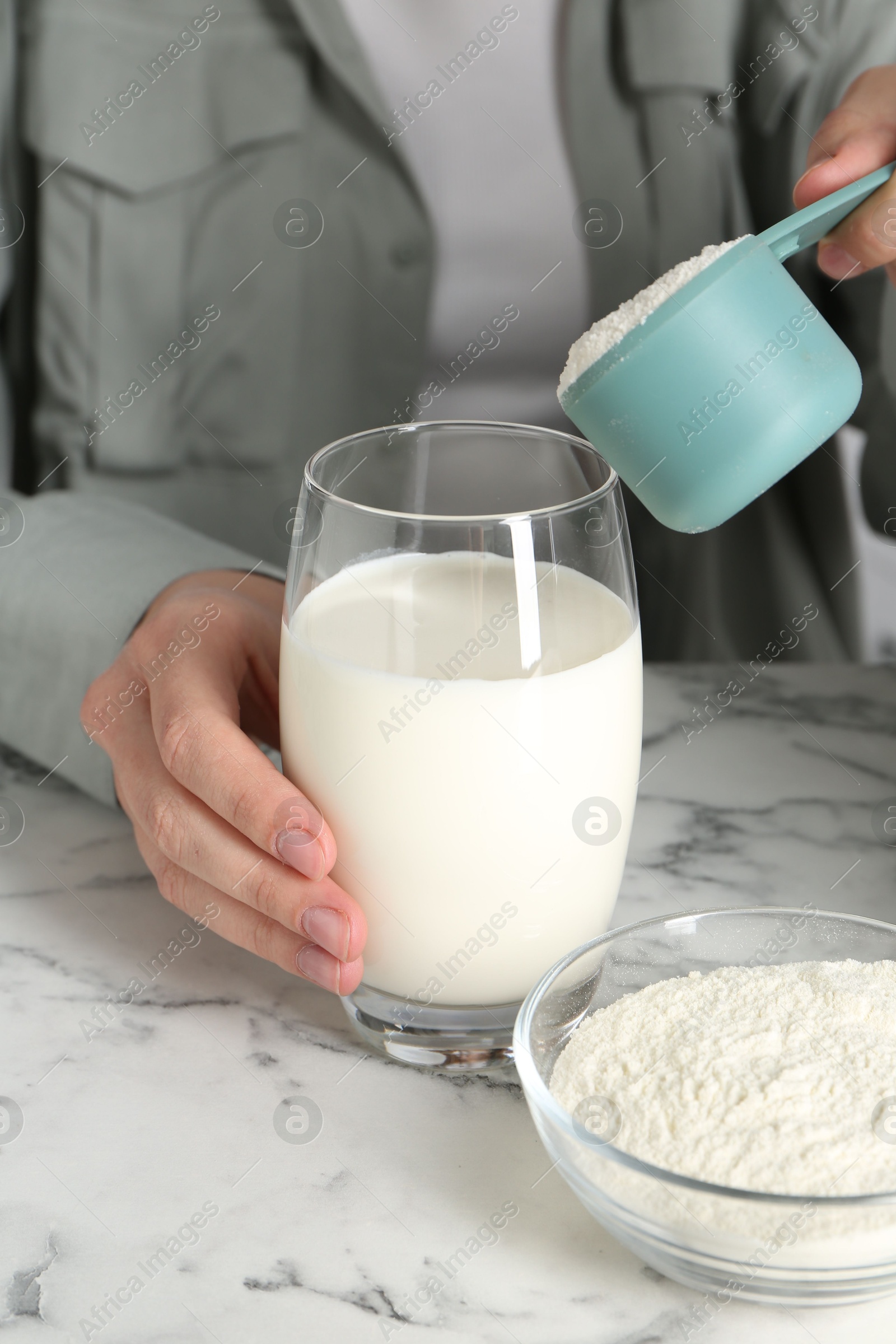 Photo of Making protein cocktail. Woman adding powder into glass with milk at white marble table, closeup