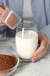 Photo of Making protein cocktail. Woman adding powder into glass with milk at white marble table, closeup