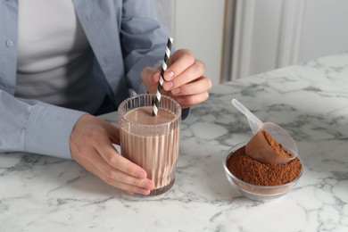 Photo of Woman with glass of protein cocktail and powder at white marble table, closeup