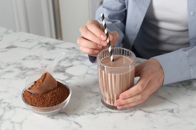 Photo of Woman with glass of protein cocktail and powder at white marble table, closeup