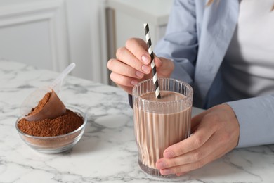 Photo of Woman with glass of protein cocktail and powder at white marble table, closeup