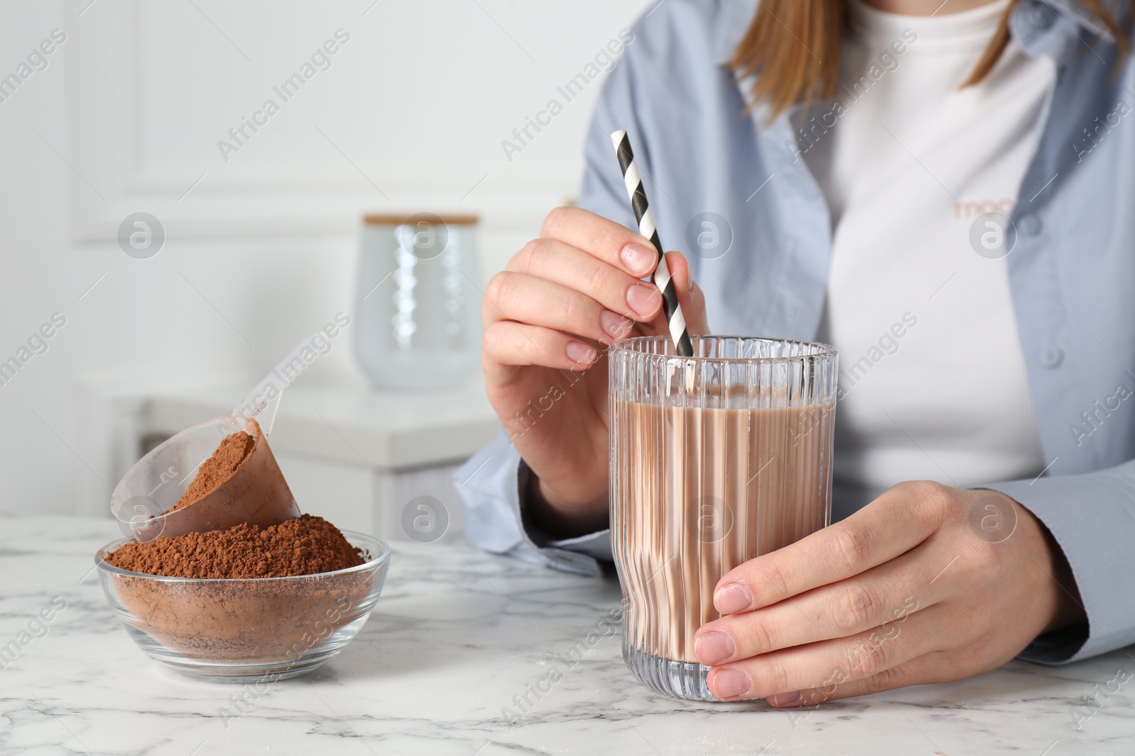 Photo of Woman with glass of protein cocktail and powder at white marble table, closeup