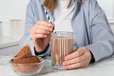 Photo of Woman with glass of protein cocktail and powder at white marble table, closeup