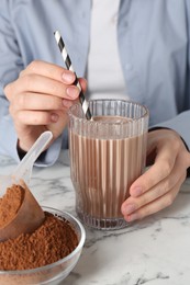 Photo of Woman with glass of protein cocktail and powder at white marble table, closeup