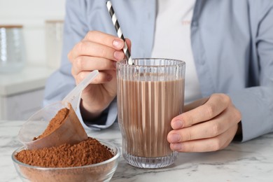 Photo of Woman with glass of protein cocktail and powder at white marble table, closeup