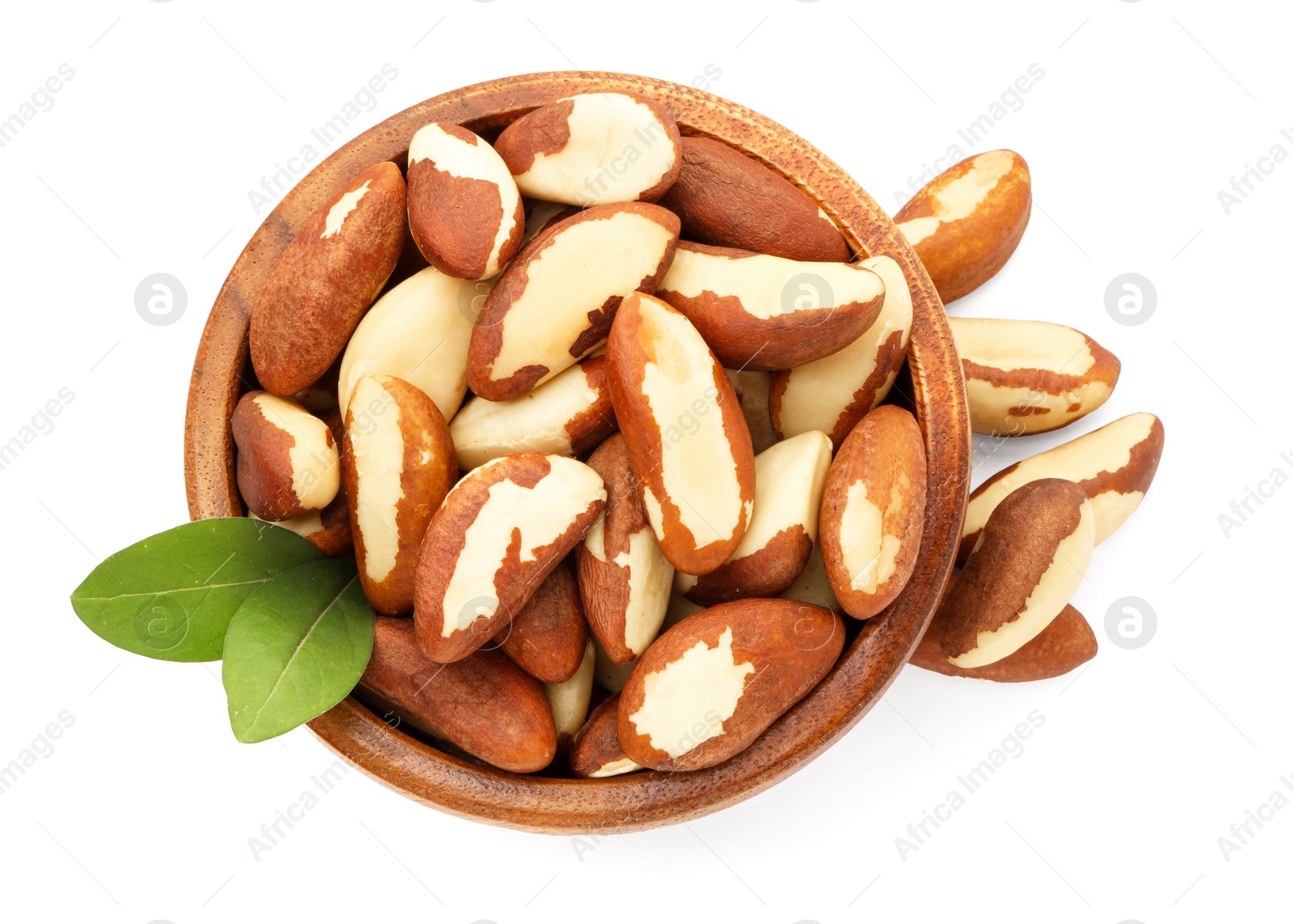 Photo of Tasty Brazil nuts and green leaves in bowl isolated on white, top view