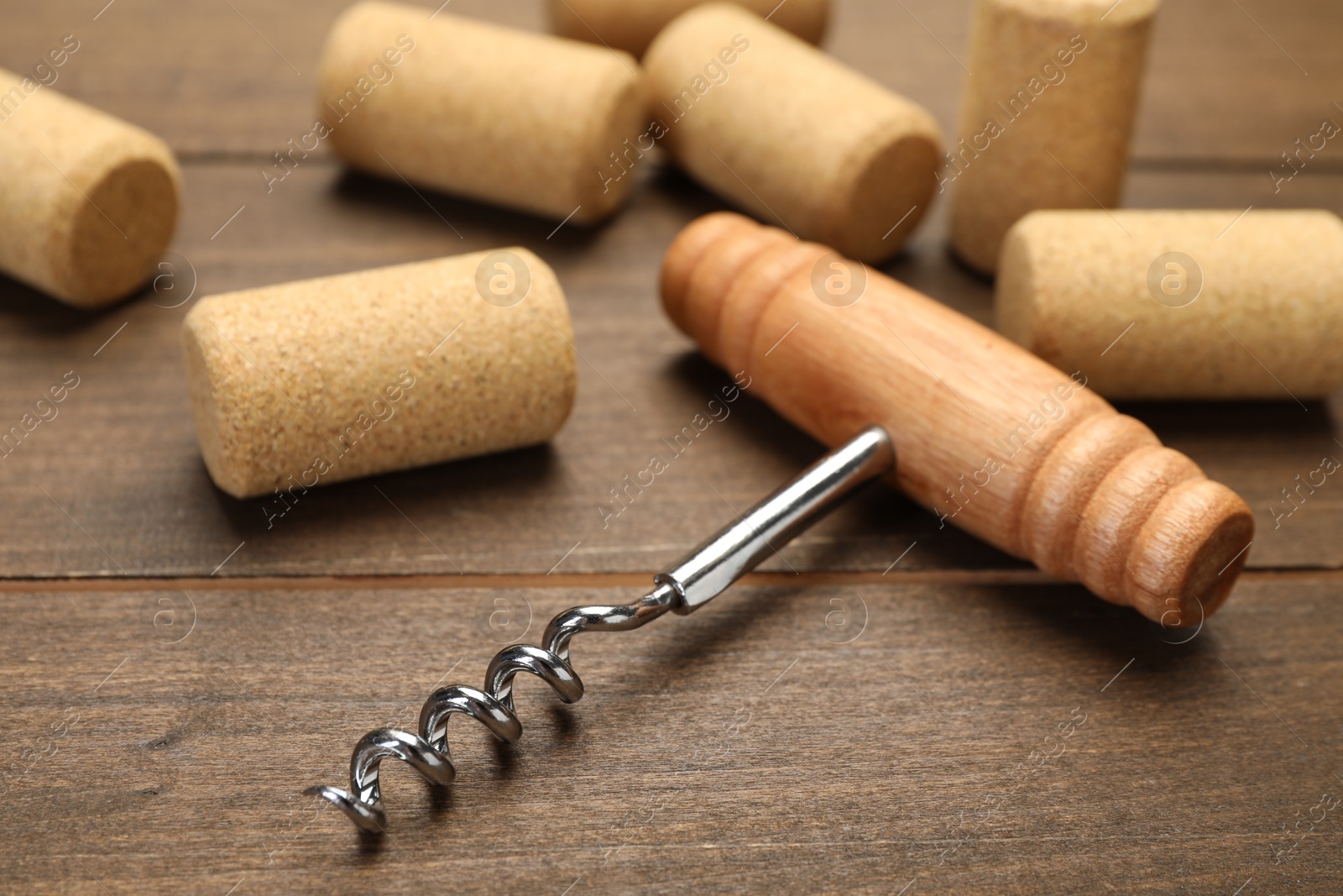 Photo of Corkscrew with handle and corks on wooden table, closeup