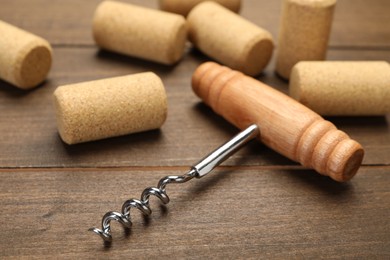 Corkscrew with handle and corks on wooden table, closeup