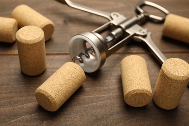 Photo of Wing corkscrew and corks on wooden table, closeup