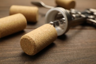 Photo of Wing corkscrew and corks on wooden table, closeup