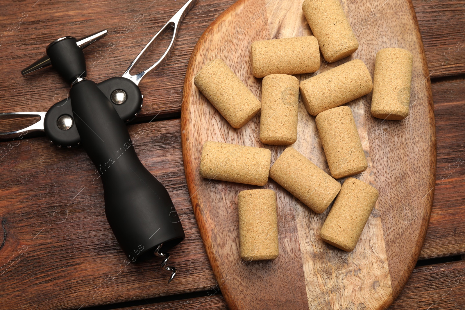 Photo of Wing corkscrew and corks on wooden table, flat lay