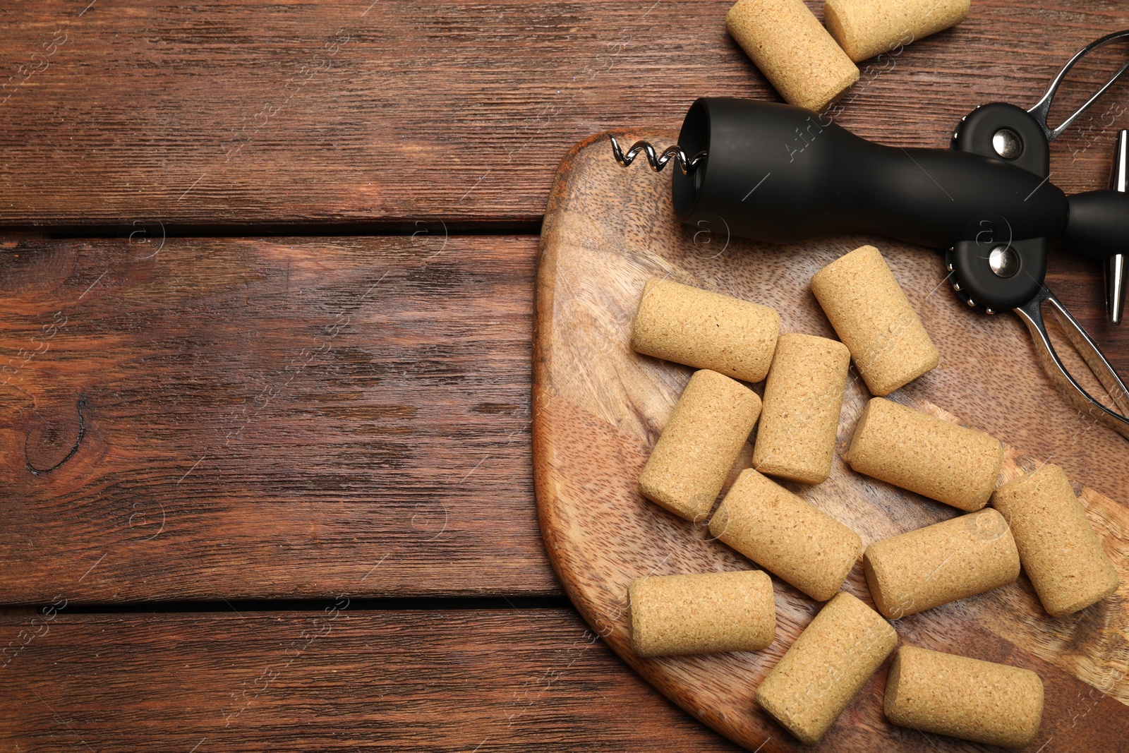 Photo of Wing corkscrew and corks on wooden table, flat lay. Space for text