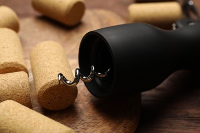 Photo of Wing corkscrew and corks on wooden table, closeup