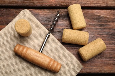 Corkscrew and corks on wooden table, flat lay