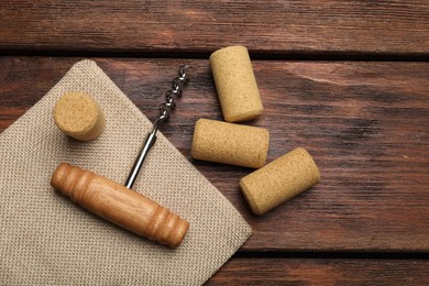 Corkscrew and corks on wooden table, flat lay