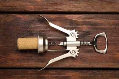 Wing corkscrew and cork on wooden table, top view