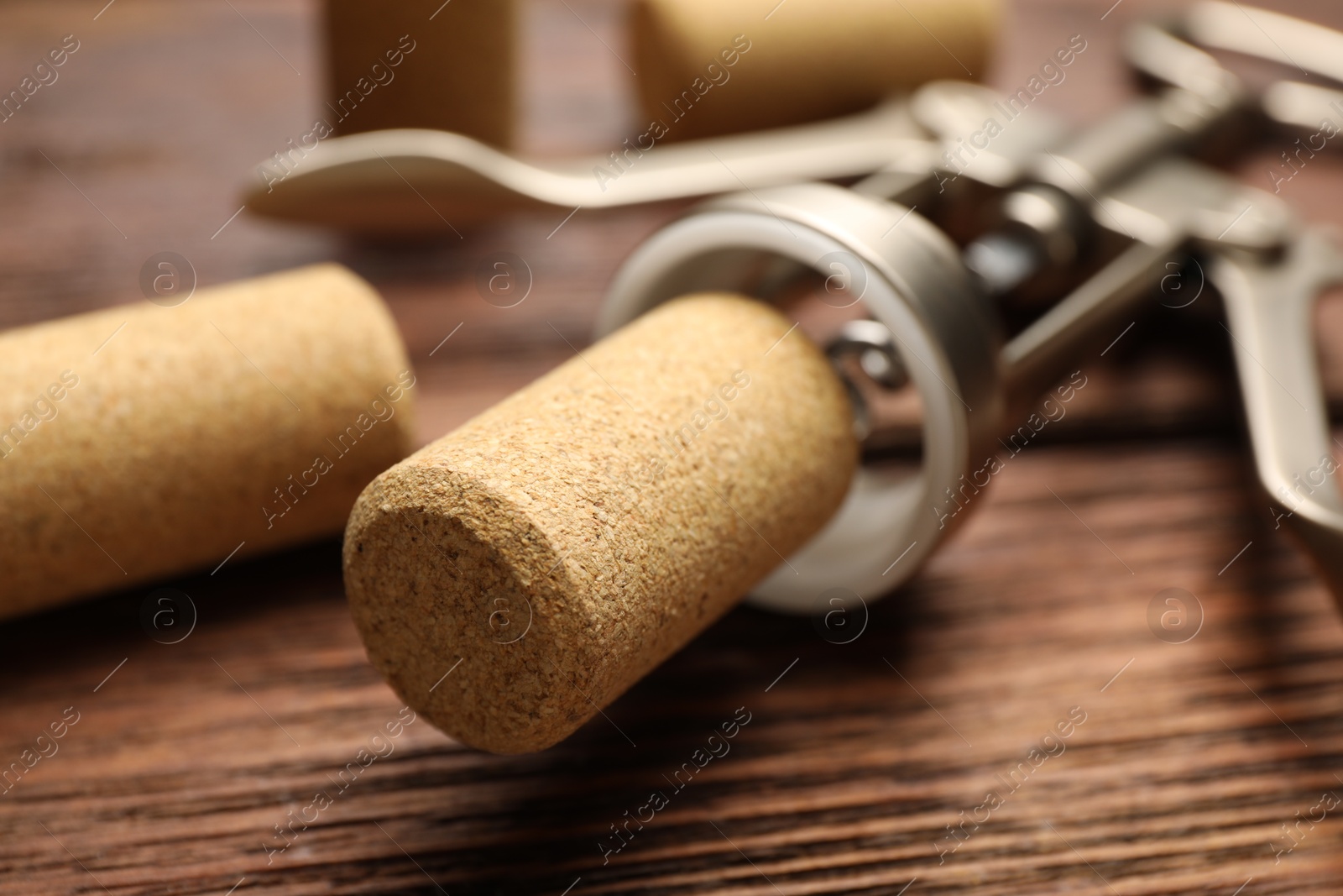 Photo of Wing corkscrew and corks on wooden table, closeup