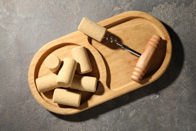 Corkscrew and corks on grey table, top view