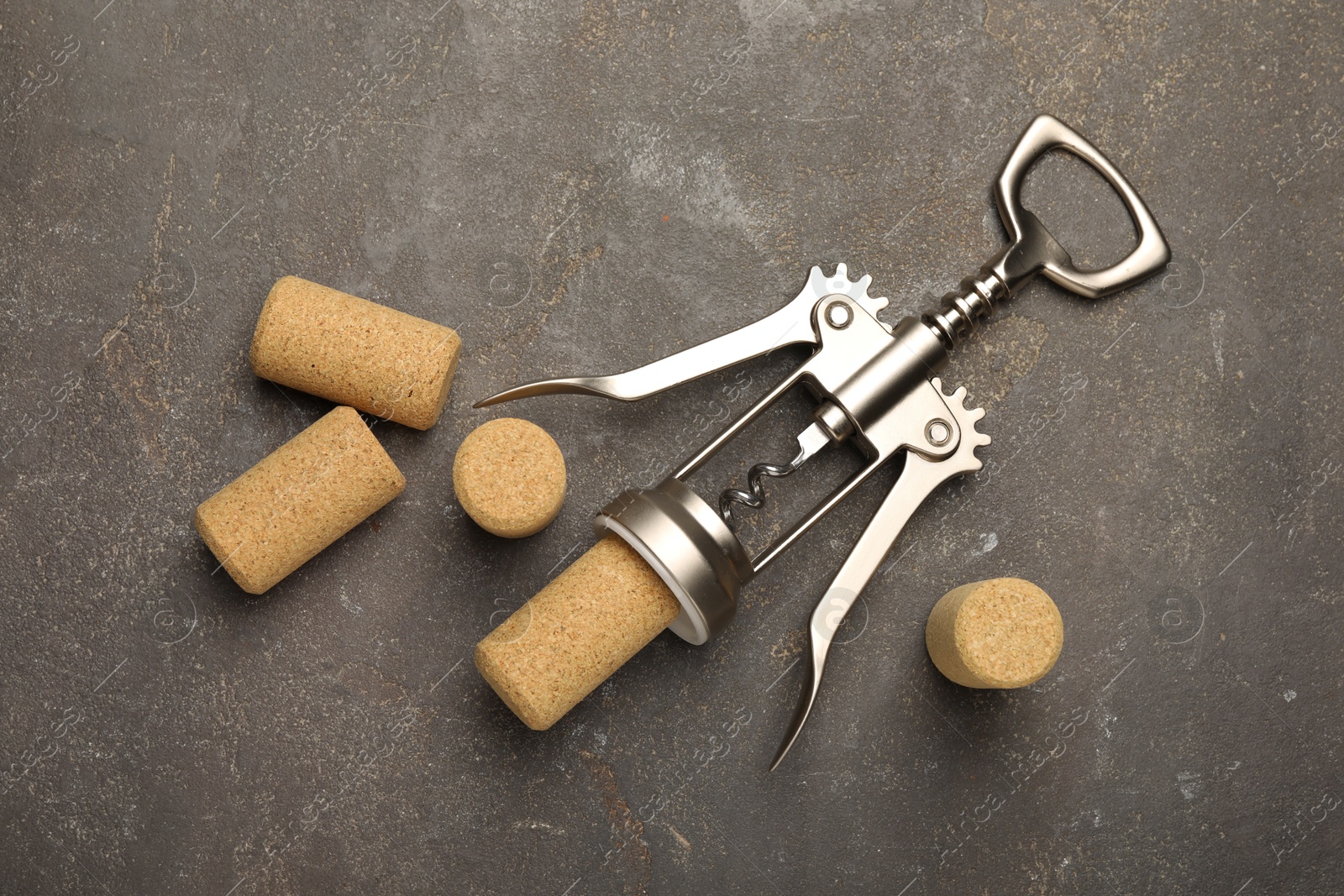 Photo of Wing corkscrew and corks on grey table, flat lay