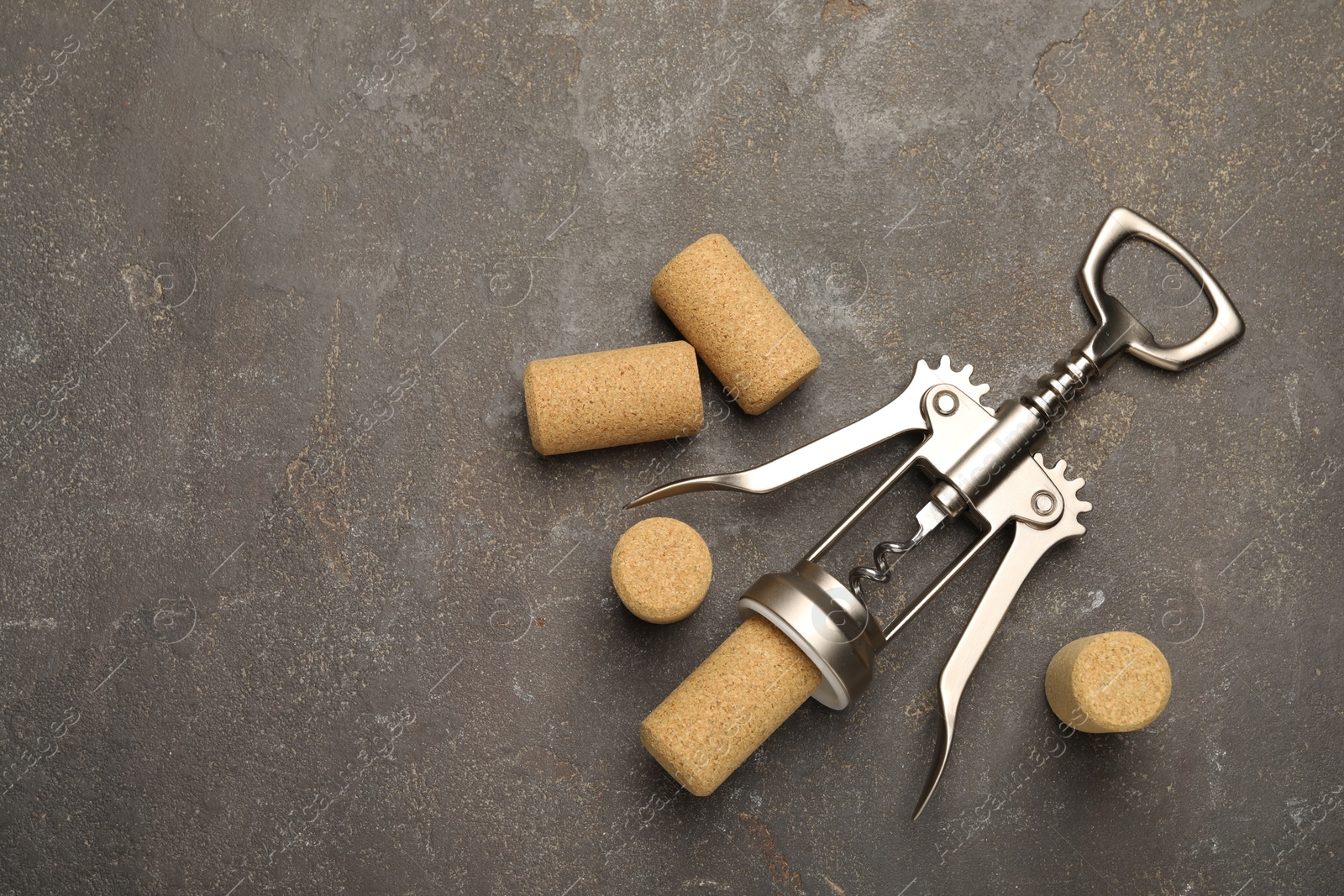 Photo of Wing corkscrew and corks on grey table, flat lay. Space for text