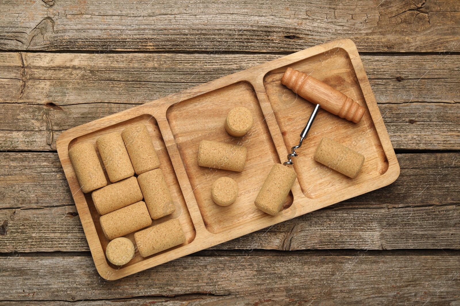 Photo of Corkscrew and corks on wooden table, top view