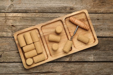 Corkscrew and corks on wooden table, top view