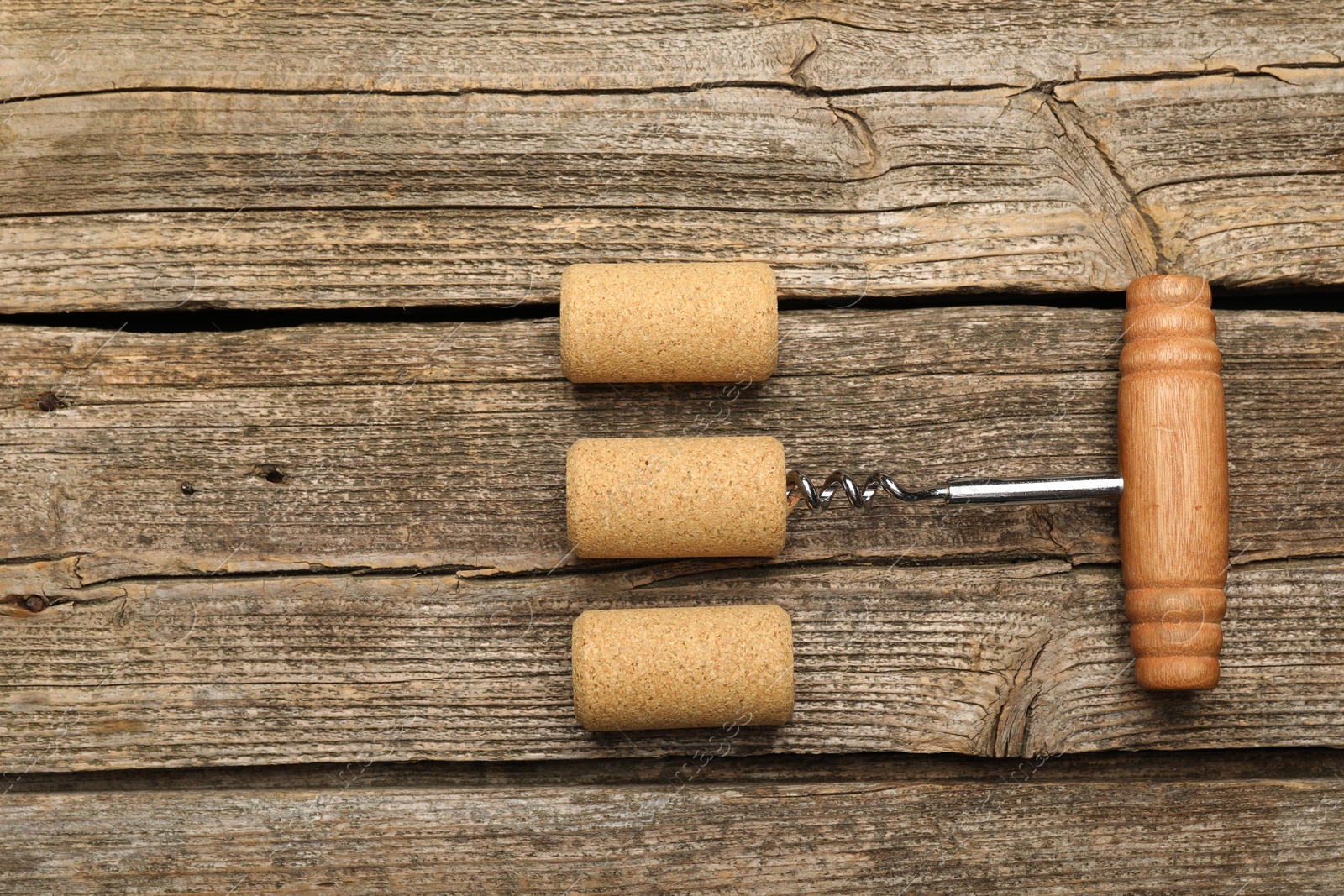 Photo of Corkscrew and corks on wooden table, flat lay. Space for text