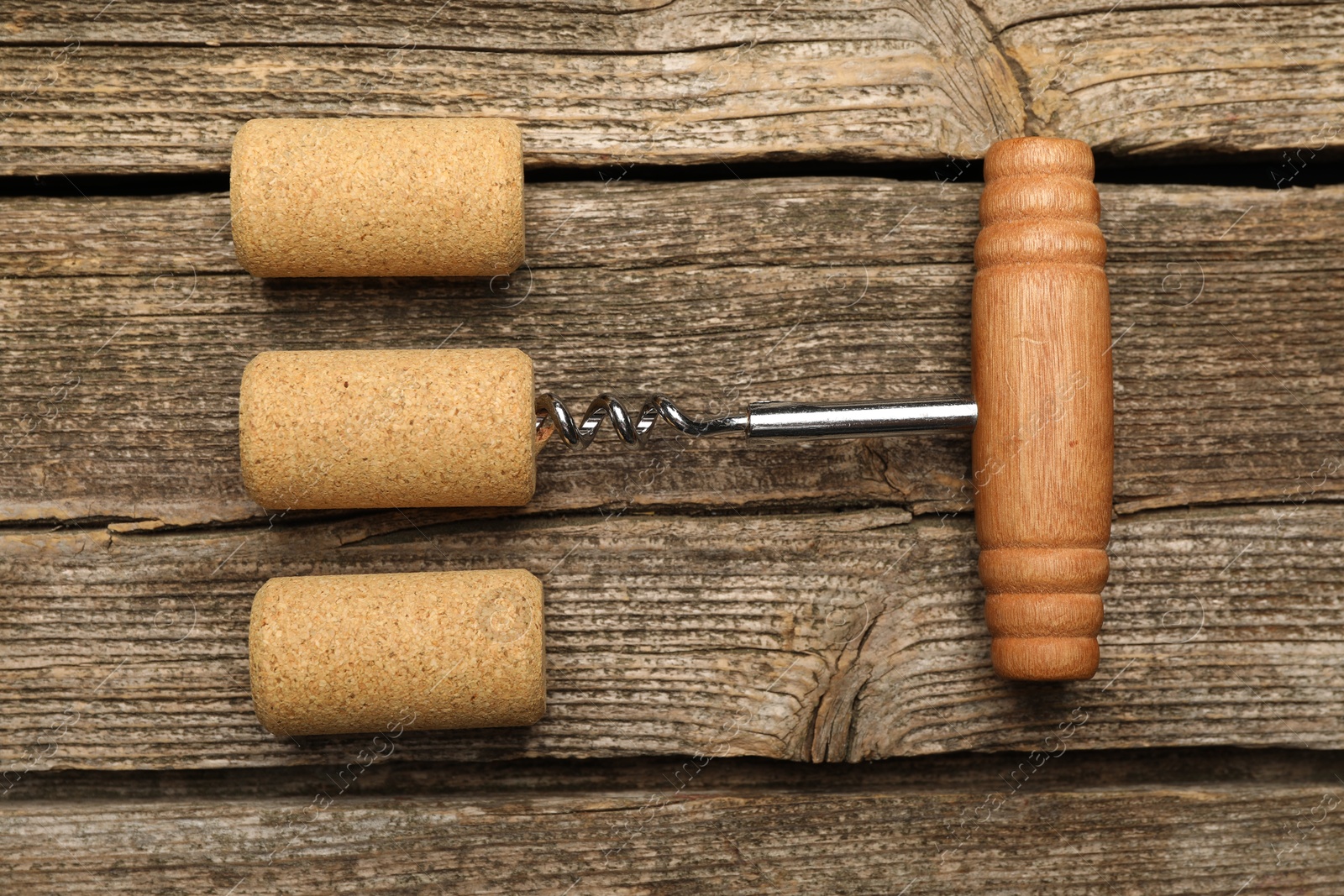 Photo of Corkscrew and corks on wooden table, flat lay