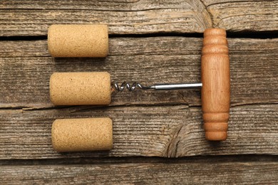 Corkscrew and corks on wooden table, flat lay