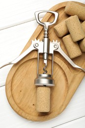 Wing corkscrew and corks on white wooden table, top view