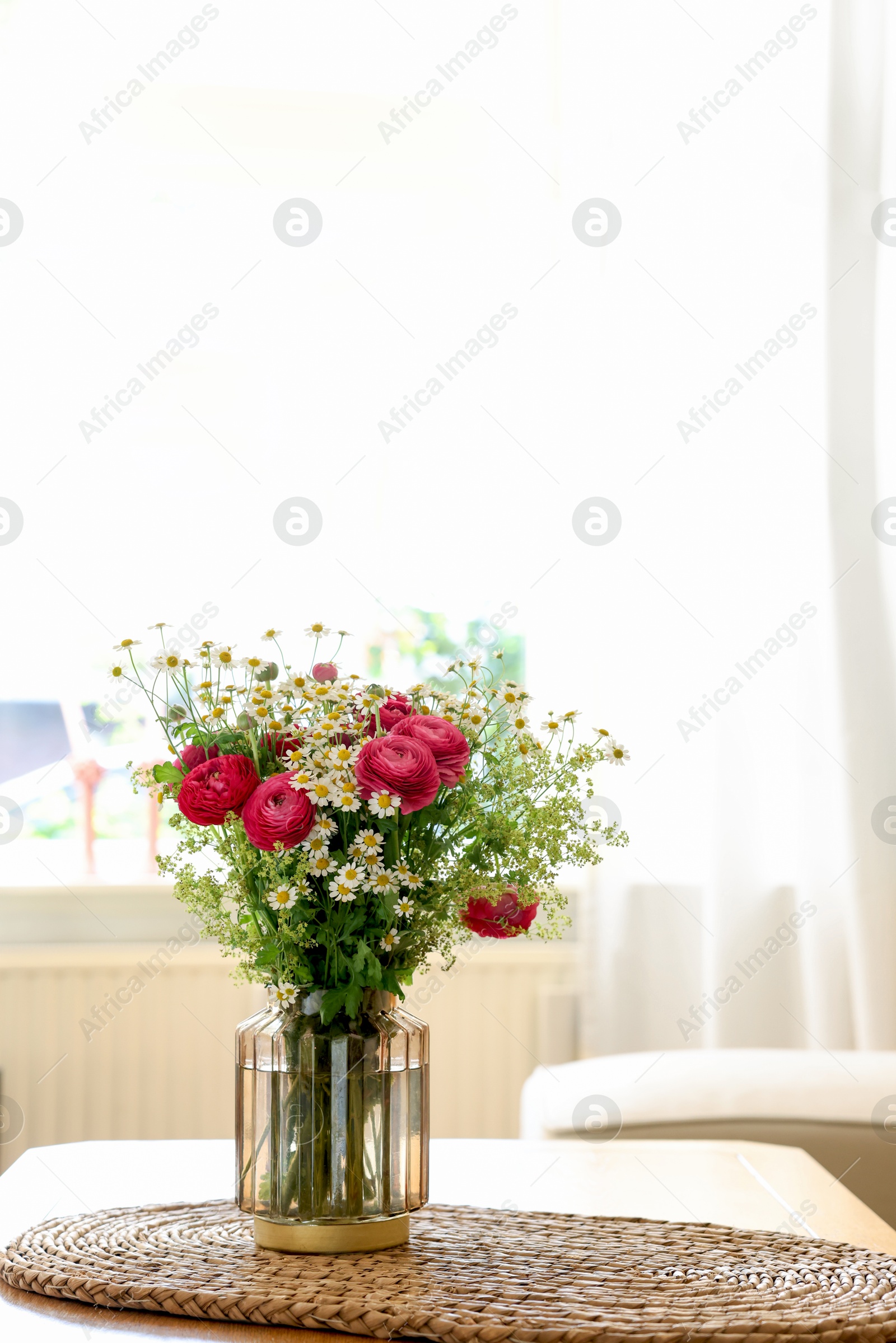 Photo of Beautiful ranunculus flowers and chamomiles in vase on table indoors