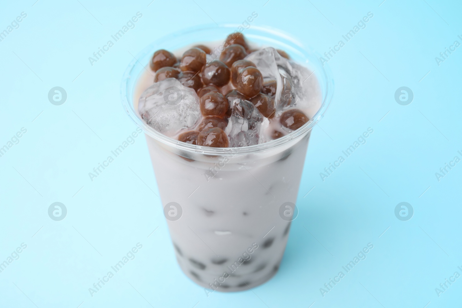 Photo of Tasty milk bubble tea in plastic cup on light blue background, closeup