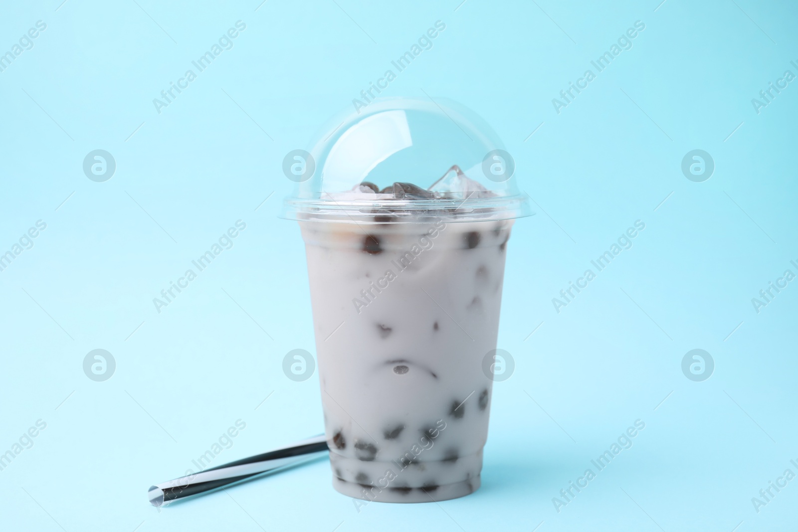 Photo of Tasty milk bubble tea in plastic cup and straws on light blue background