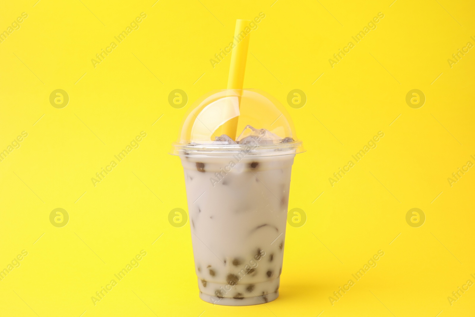 Photo of Tasty milk bubble tea in plastic cup on yellow background