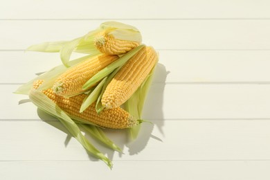 Photo of Many fresh ripe corncobs with green husks on white wooden table, top view. Space for text