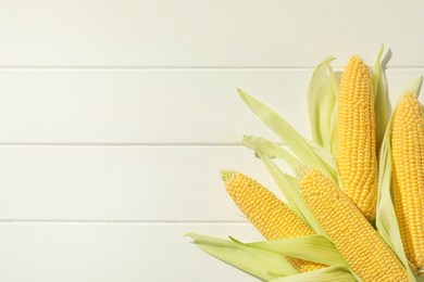 Photo of Many fresh ripe corncobs with green husks on white wooden table, top view. Space for text