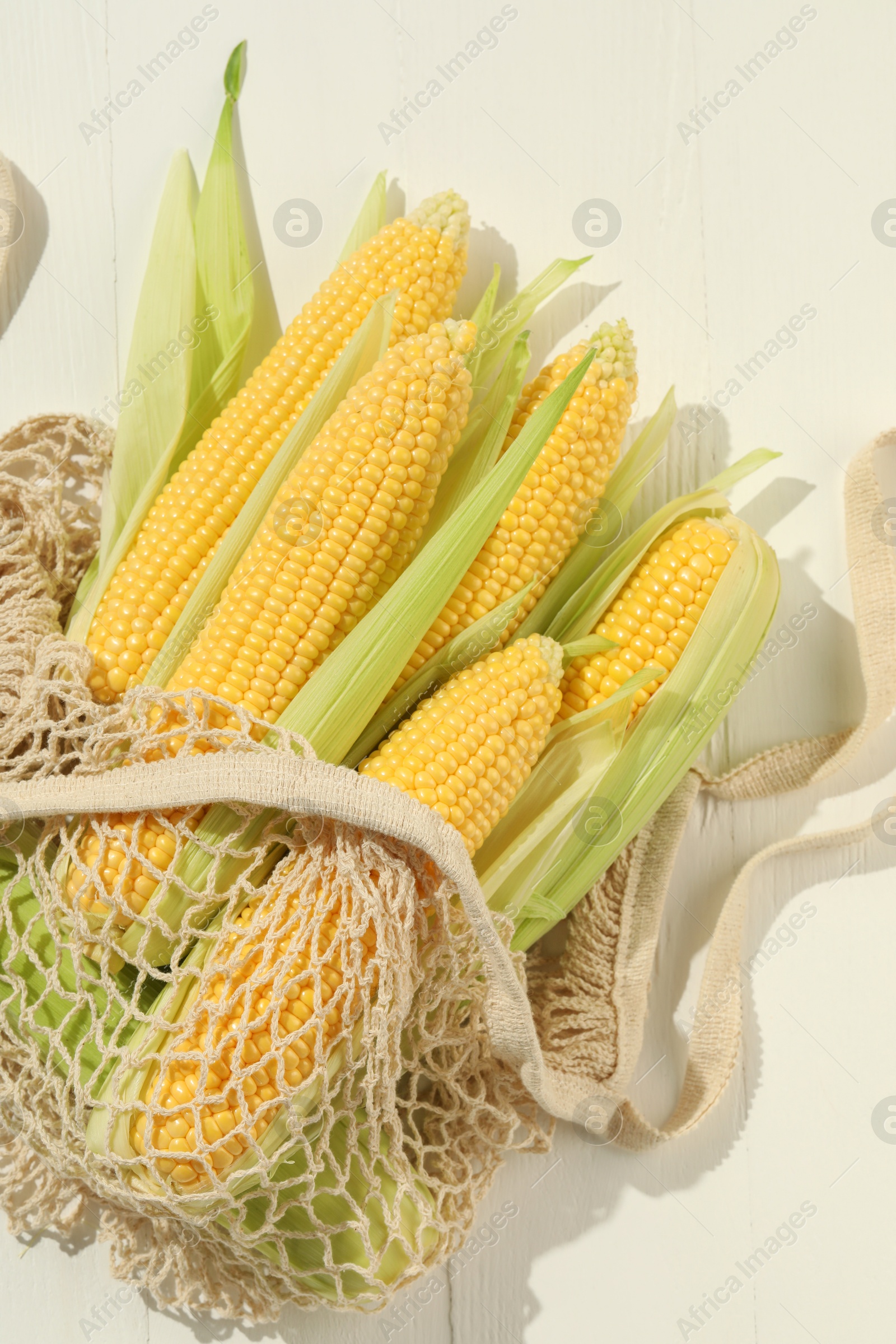 Photo of Many fresh ripe corncobs with green husks on white wooden table, top view