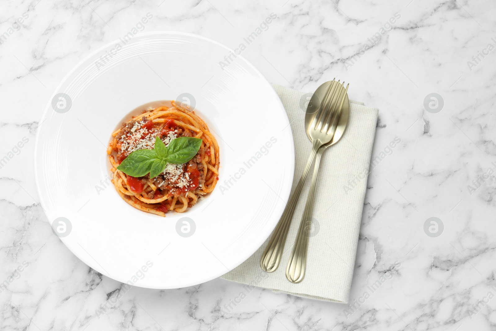 Photo of Delicious pasta bolognese with basil and cutlery on white marble table, top view