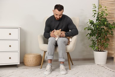 Man petting cute ginger cat on armchair at home