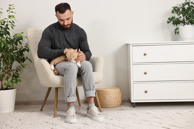 Man petting cute ginger cat on armchair at home