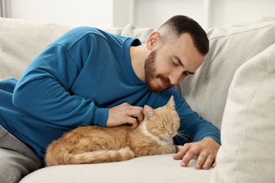 Photo of Man petting cute ginger cat on sofa at home