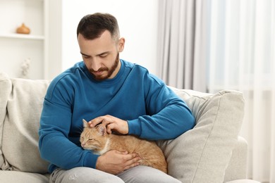 Photo of Man petting cute ginger cat on sofa at home