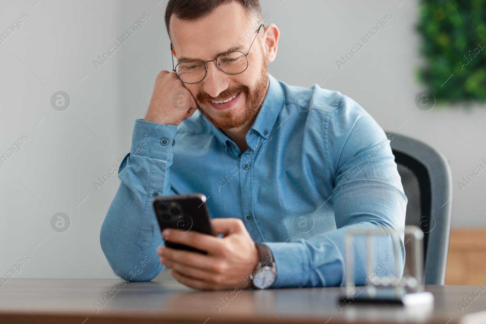 Photo of Smiling man looking at smartphone in office